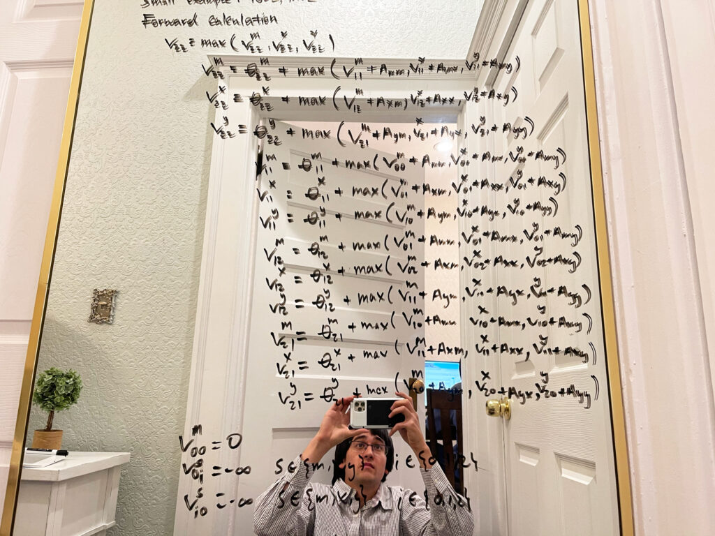 A photo of Jamie Morton capturing his reflection in a mirror at home, which he’s repurposed as a makeshift whiteboard filled with equations.
