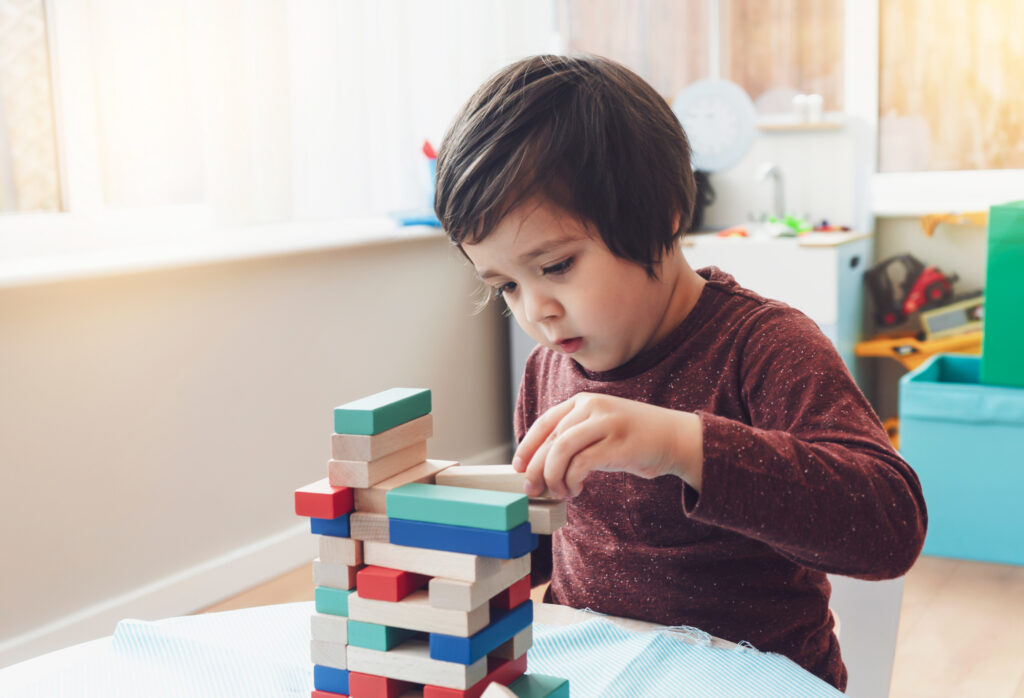 A candid shot of cheerful little boy plays colorful wooden blocks in play room.