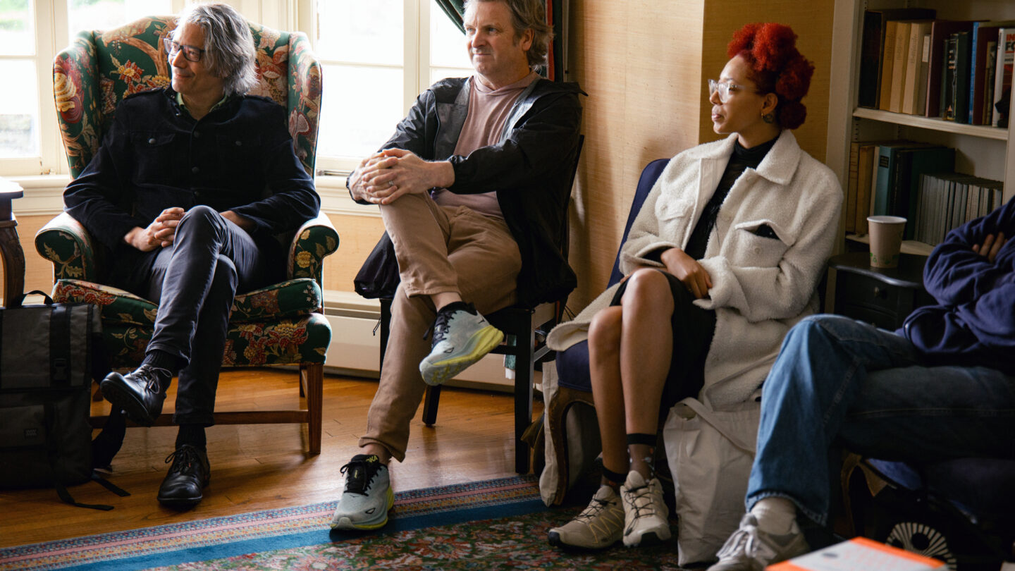 Three people sitting on chairs in and part of group discussion.
