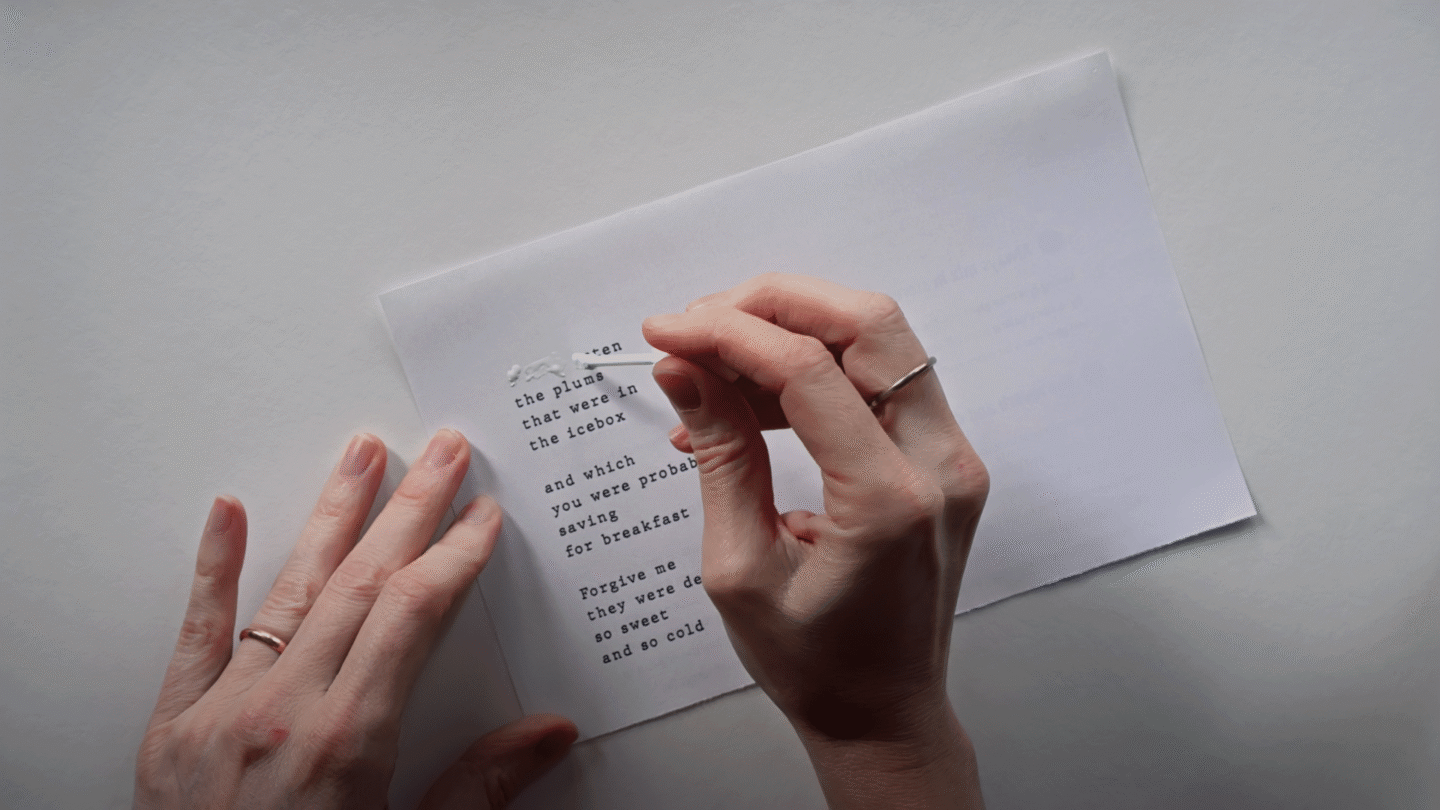 Two hands, one holding a paper while the other applies whiteout to text set like a poem.
