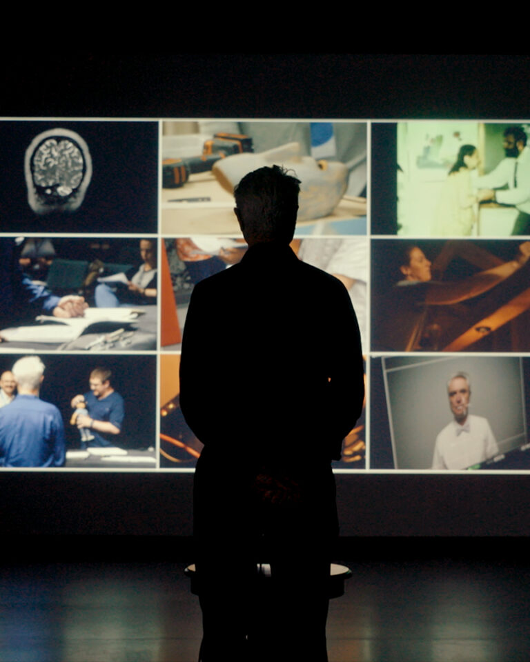 A person stands in a dark room, silhouetted against a large screen displaying eight images, including medical scans, people interacting, and scientific activities.