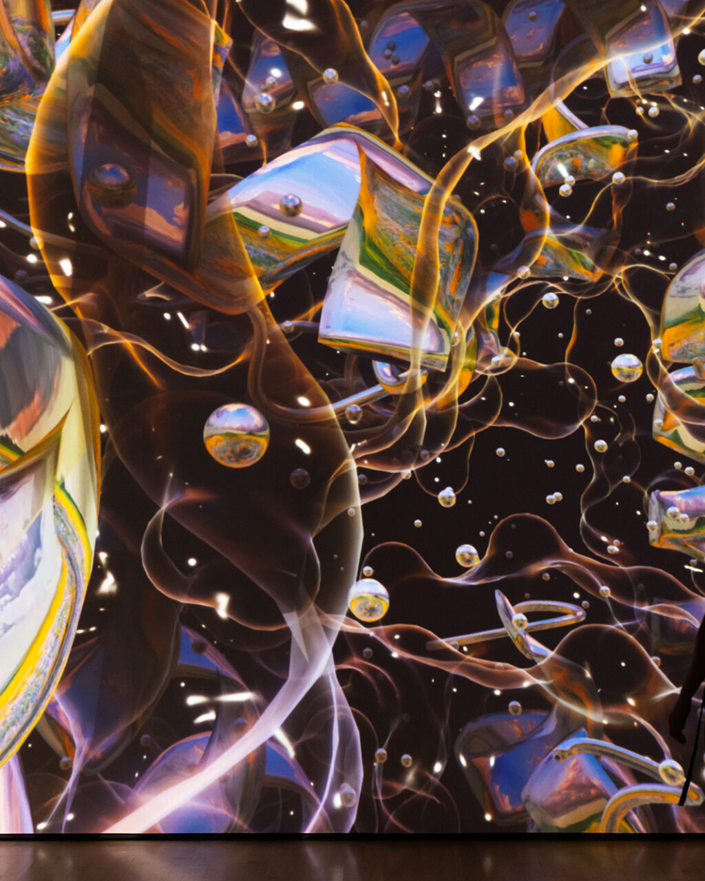 A person stands in front of a large, colorful digital art display featuring abstract swirling shapes, reflections, and floating bubbles against a dark background.