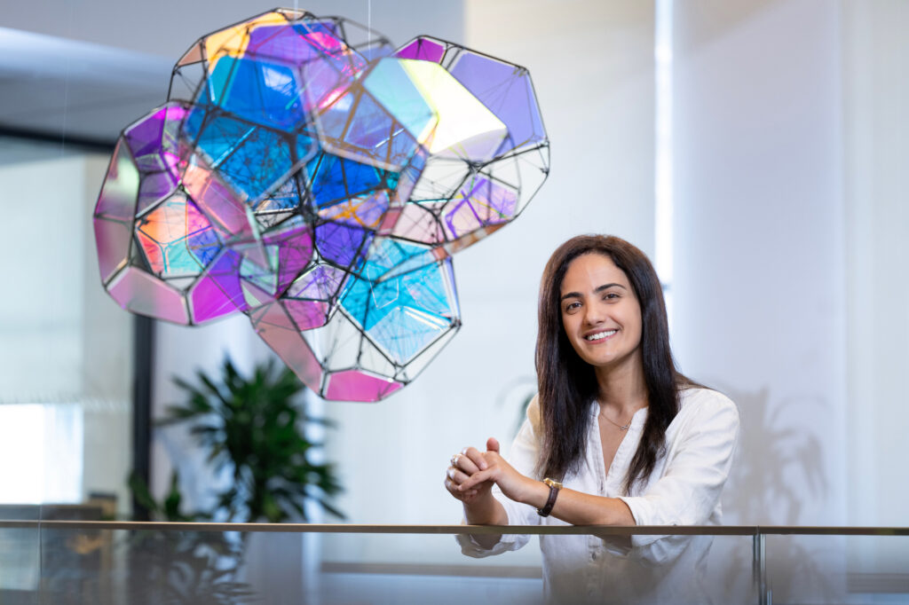 A photo of Nour Hassanieh standing in front of colorful sculpture.