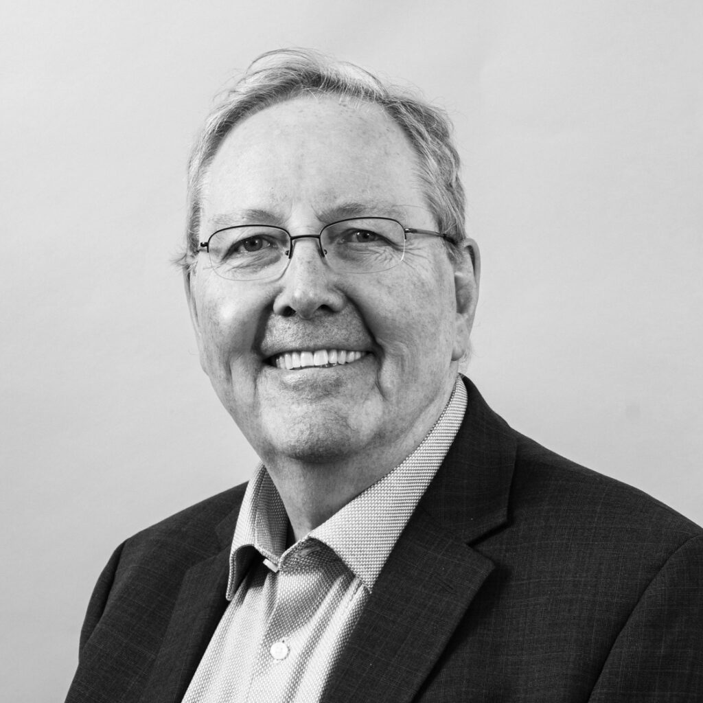 Portrait of Peter Littlewood on a plain backdrop, wearing a suit and smiling.