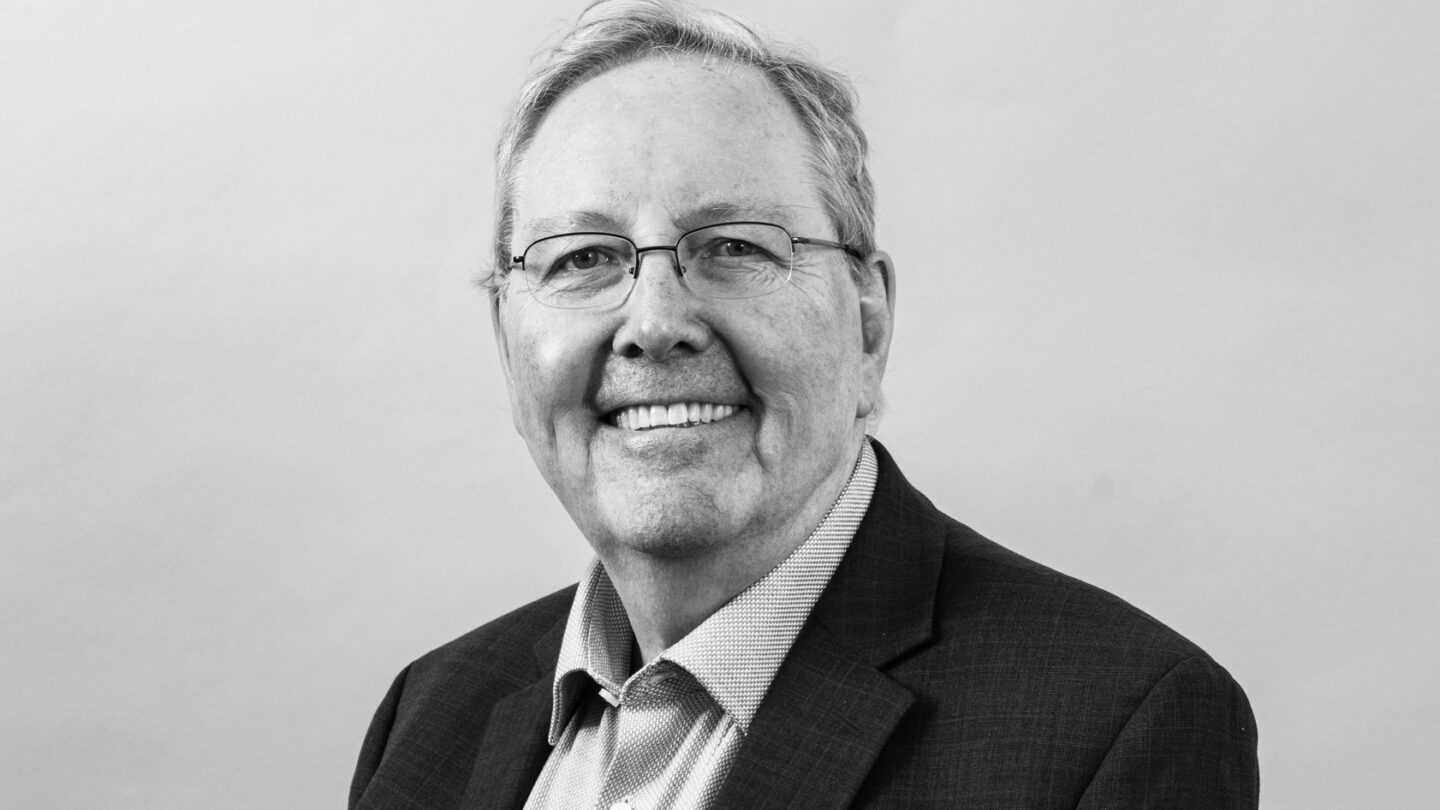 Portrait of Peter Littlewood on a plain backdrop, wearing a suit and smiling.