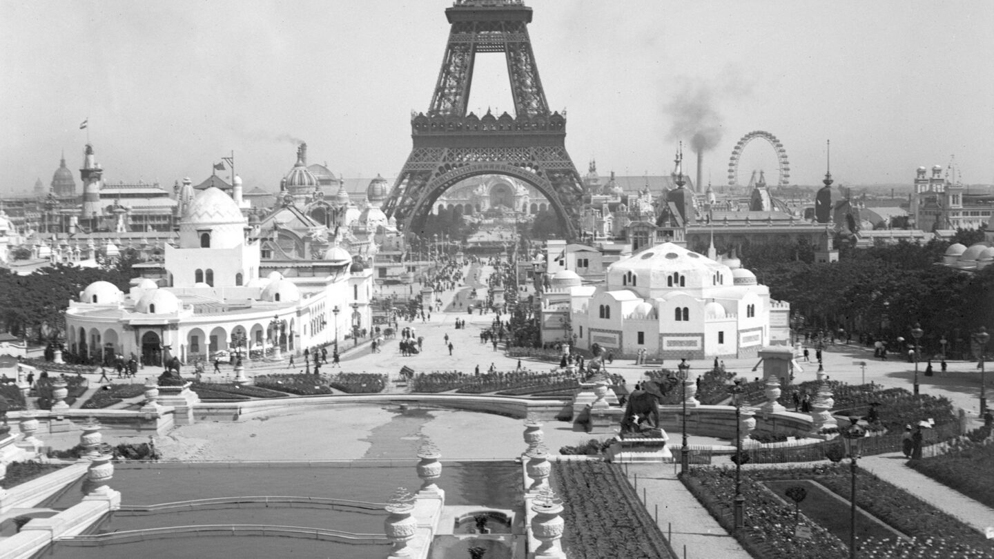 Black and white photo of the Eiffel Tower with a ferris wheel in the background.