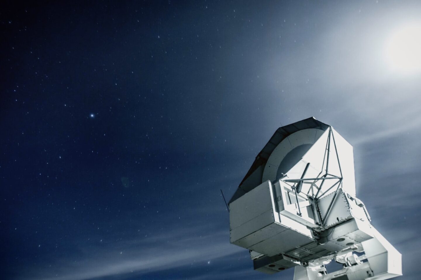 A large radio telescope points toward a starry night sky with the moon shining brightly in the upper right corner.