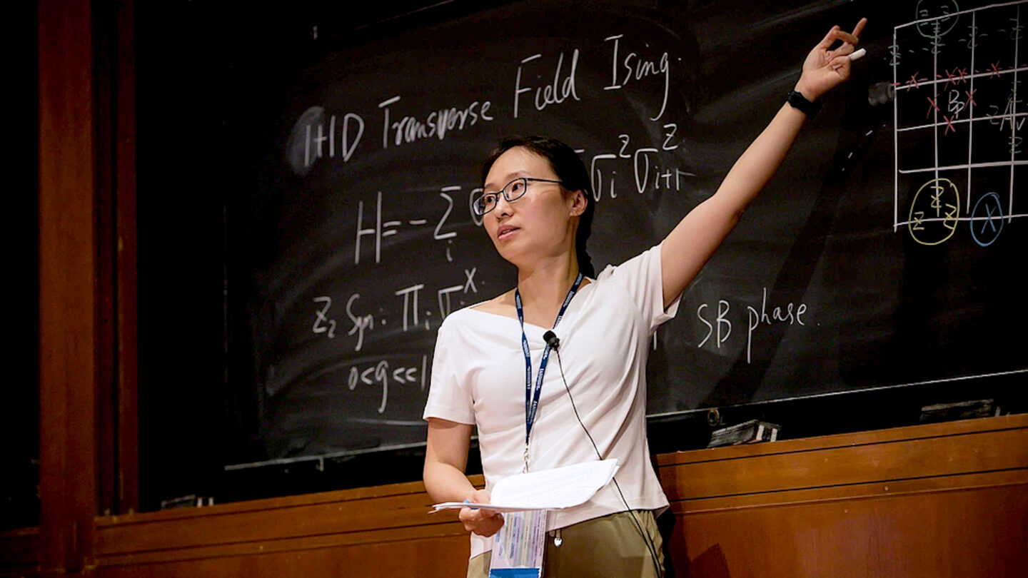 A photo of Xie Chen presenting in front of a large chalkboard.