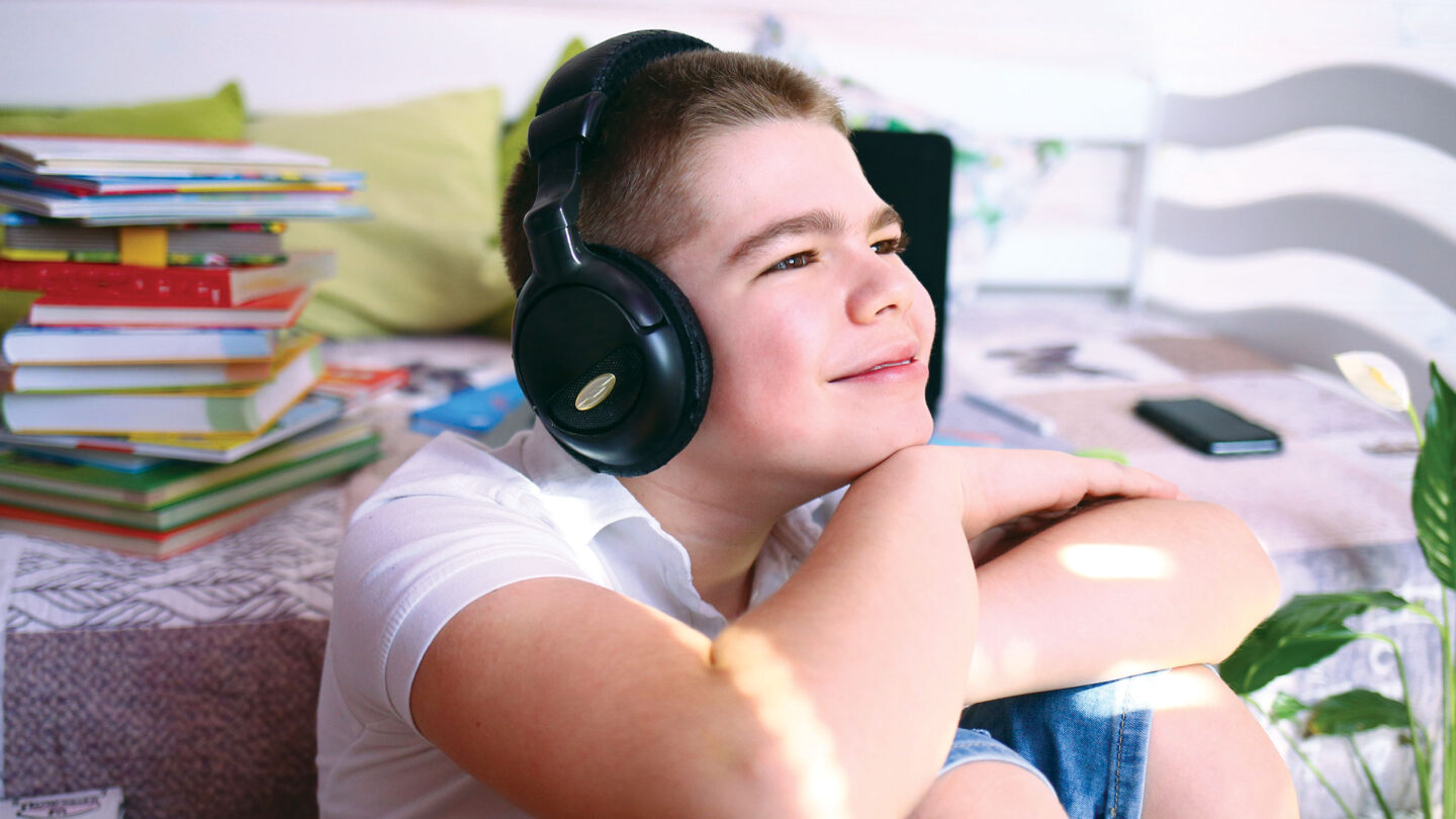 A smiling boy wearing black headphones rests his chin on his hands.