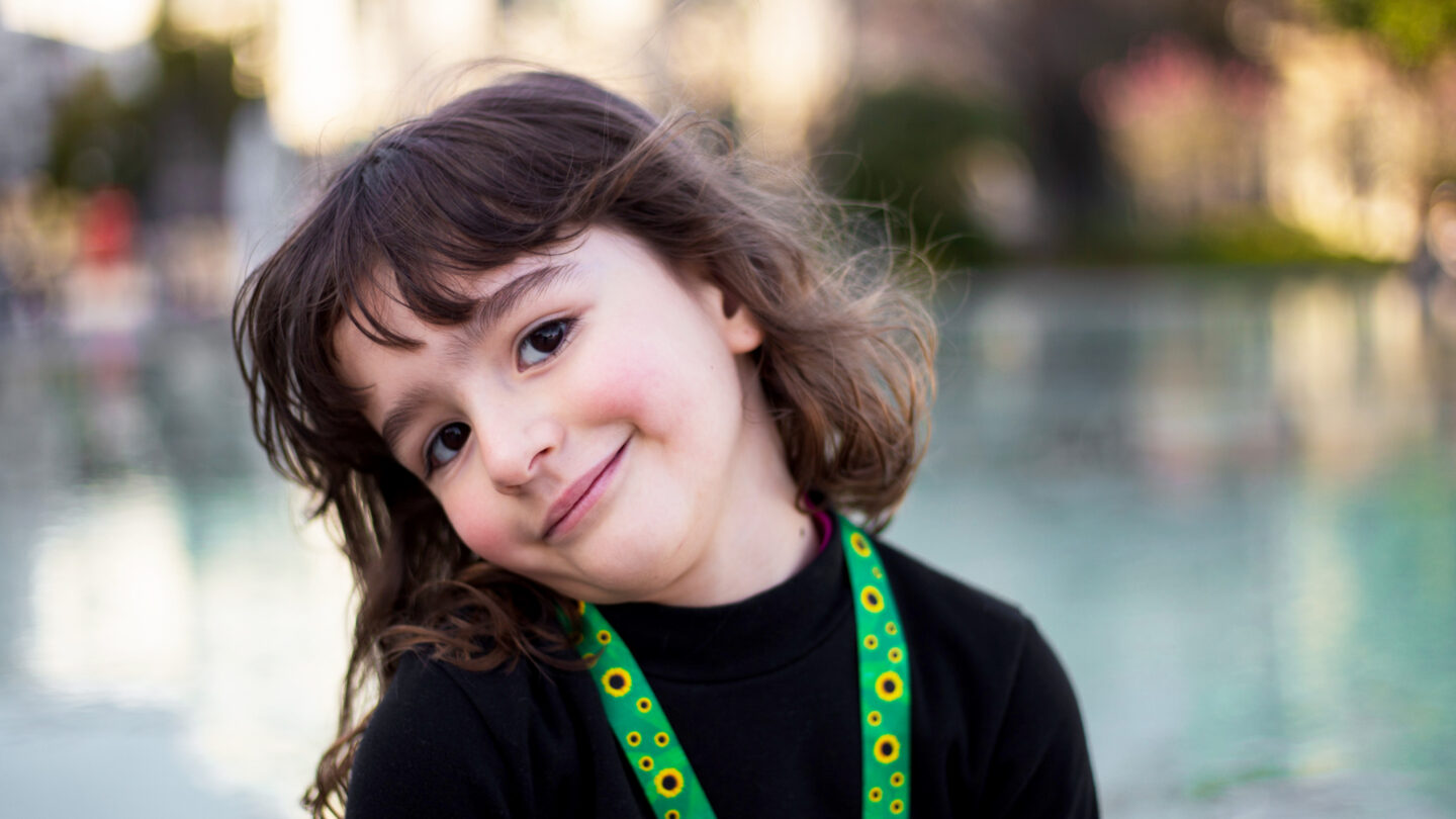 Photo of a cute little girl with an autism identification lanyard of sunflowers on a green background.