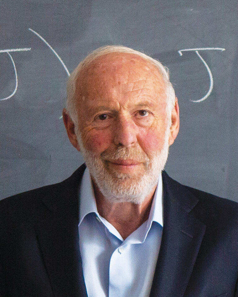 Photo of Jim Simons in front of a chalk board that shows an equation.