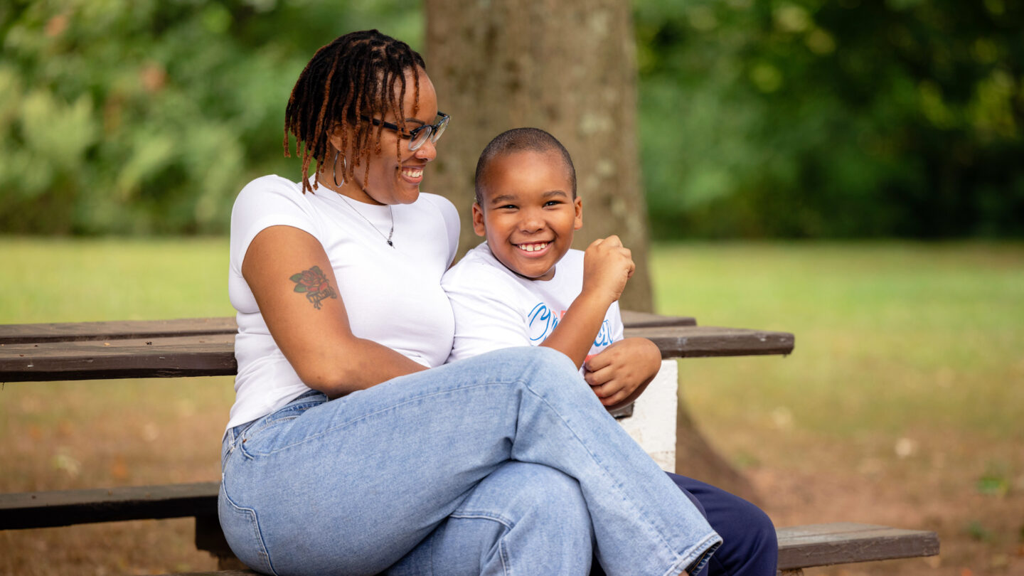 A photo of a smiling young boy with a smiling woman sitting on a bench.