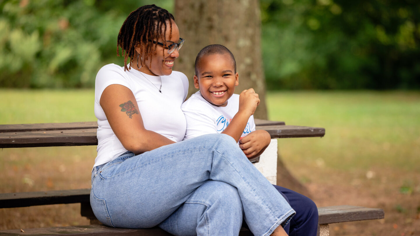 A photo of a smiling young boy with a smiling woman sitting on a bench.