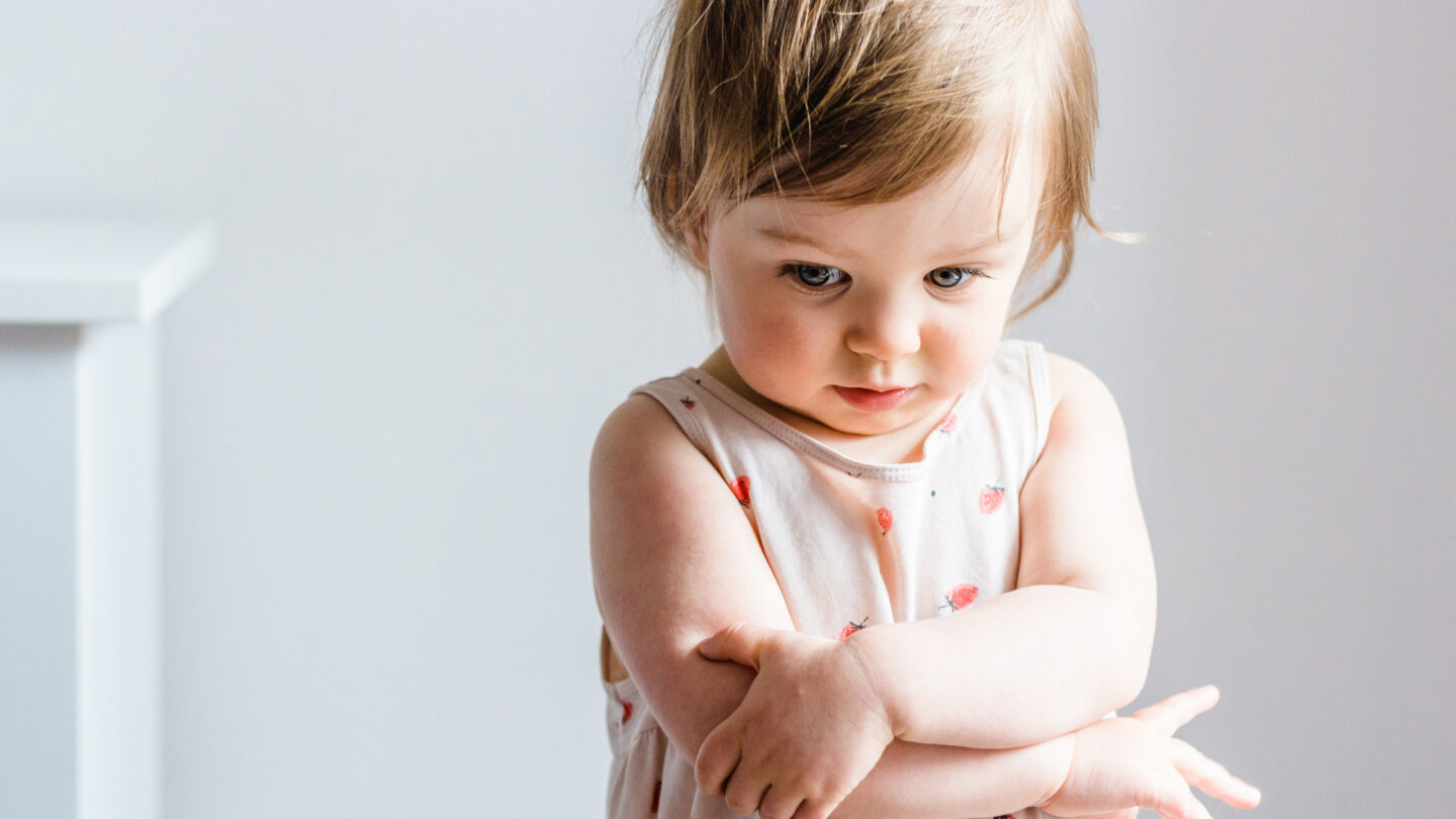 Sad or angry toddler baby girl looking down with her arms crossed.