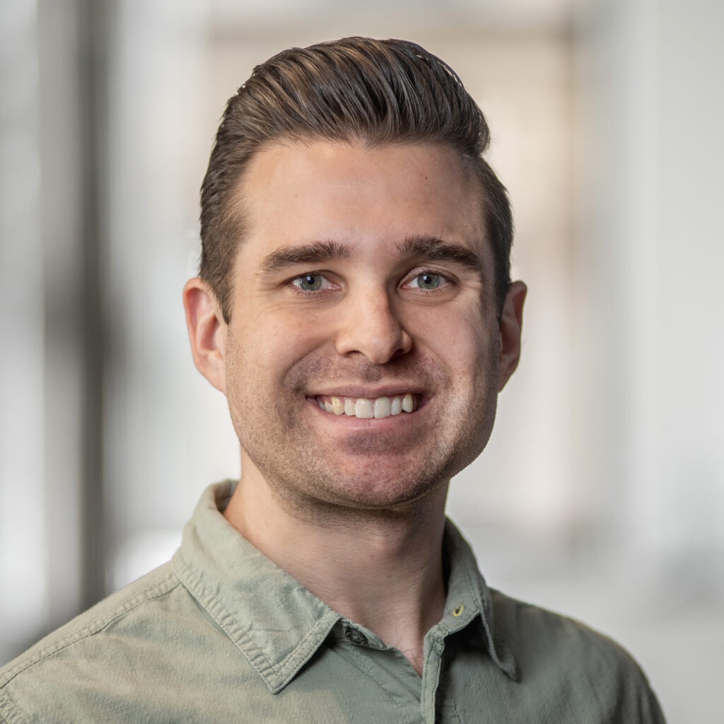 A headshot of a smiling man in a light green shirt.