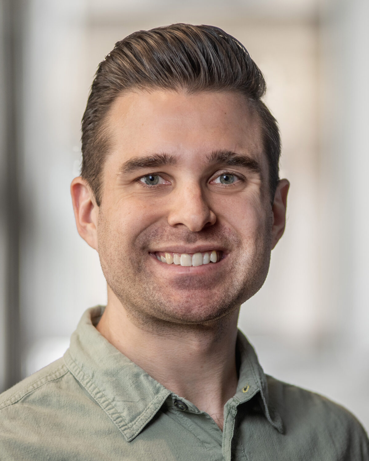 A headshot of a smiling man in a light green shirt.