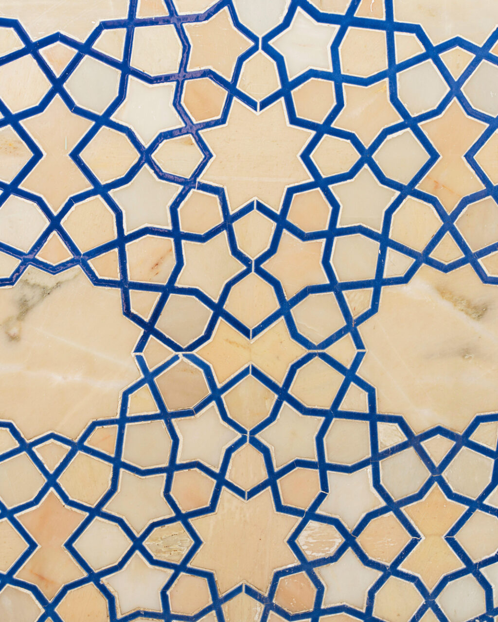 Geometric Islamic tile pattern with interlocking blue lines forming star shapes on a beige and white background.