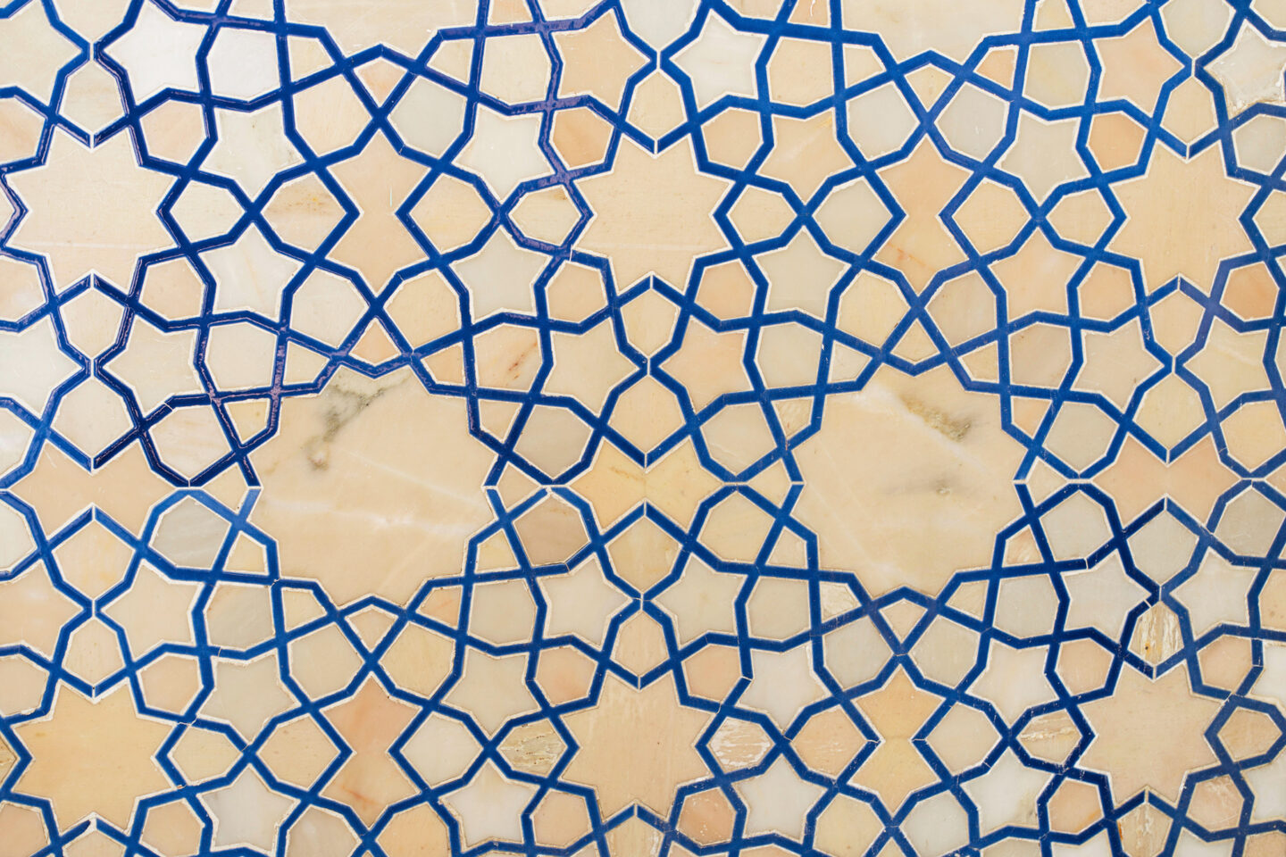 Geometric Islamic tile pattern with interlocking blue lines forming star shapes on a beige and white background.