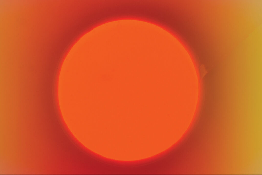 A bright orange circle centered against a gradient background shifting from deep red to yellow.