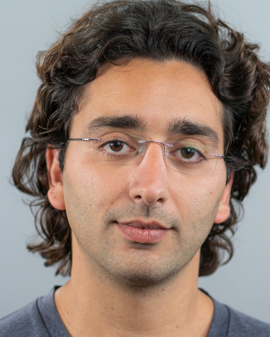 Headshot of a man with dark curly hair wearing rimless glasses.