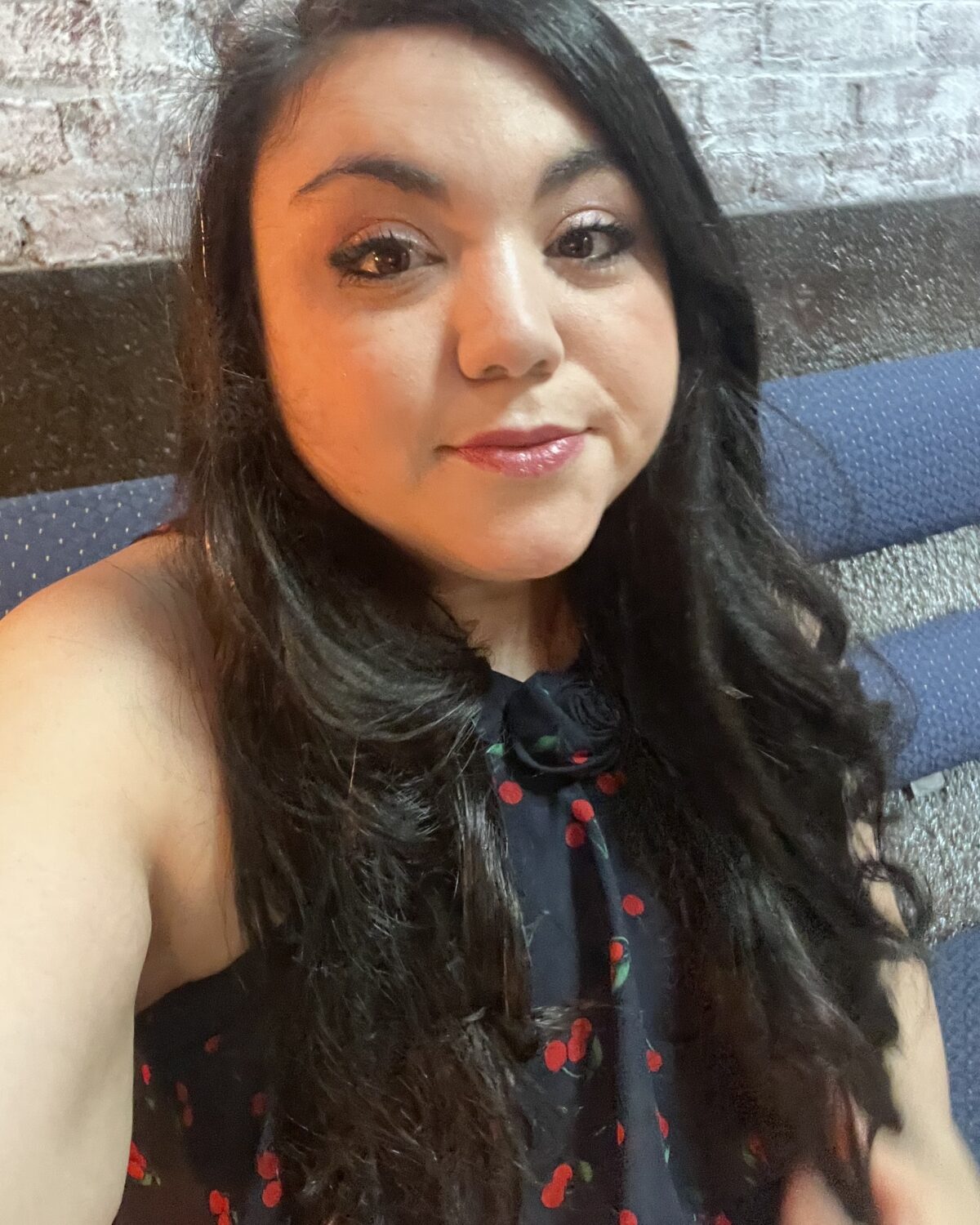 A person with long dark hair wears a navy blue top with a red cherry print.