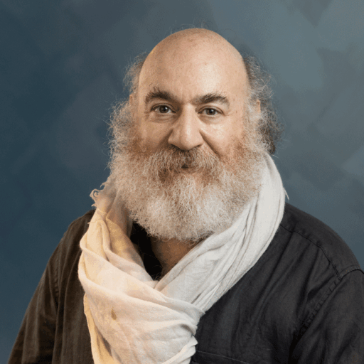 A middle-aged man with a full beard and balding head wearing a black shirt and a draped white scarf.