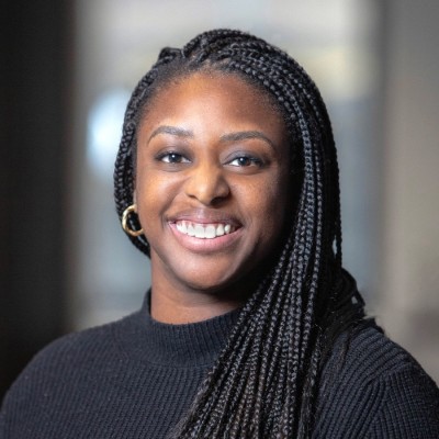 A smiling woman with braided hair wearing a black sweater.