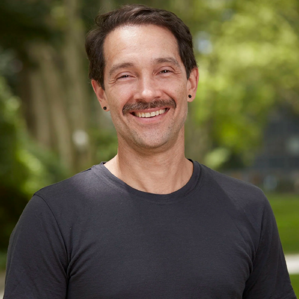 A smiling man with a mustache wearing a black t-shirt.