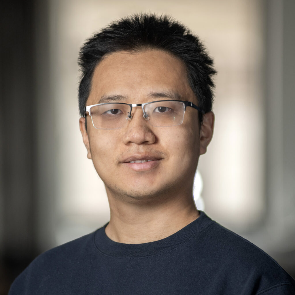 A man with short dark hair and glasses smiles slightly at the camera.