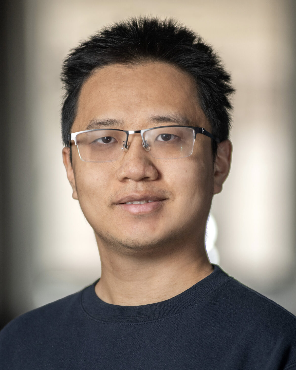A man with short dark hair and glasses smiles slightly at the camera.