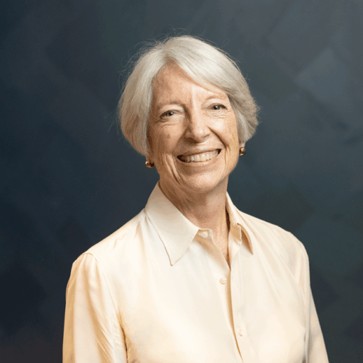 A headshot of a smiling woman with short, grey hair wearing a light-colored button-down shirt.
