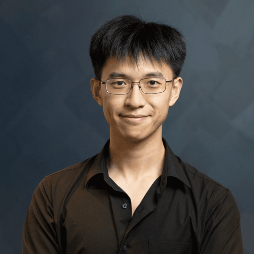 A young man with short dark hair and glasses smiles while wearing a black button-up shirt.