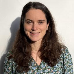 A smiling woman with long brown hair wearing a blue floral patterned top.