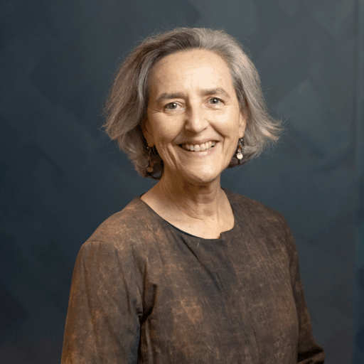 A smiling woman with gray hair wearing a dark, textured top.