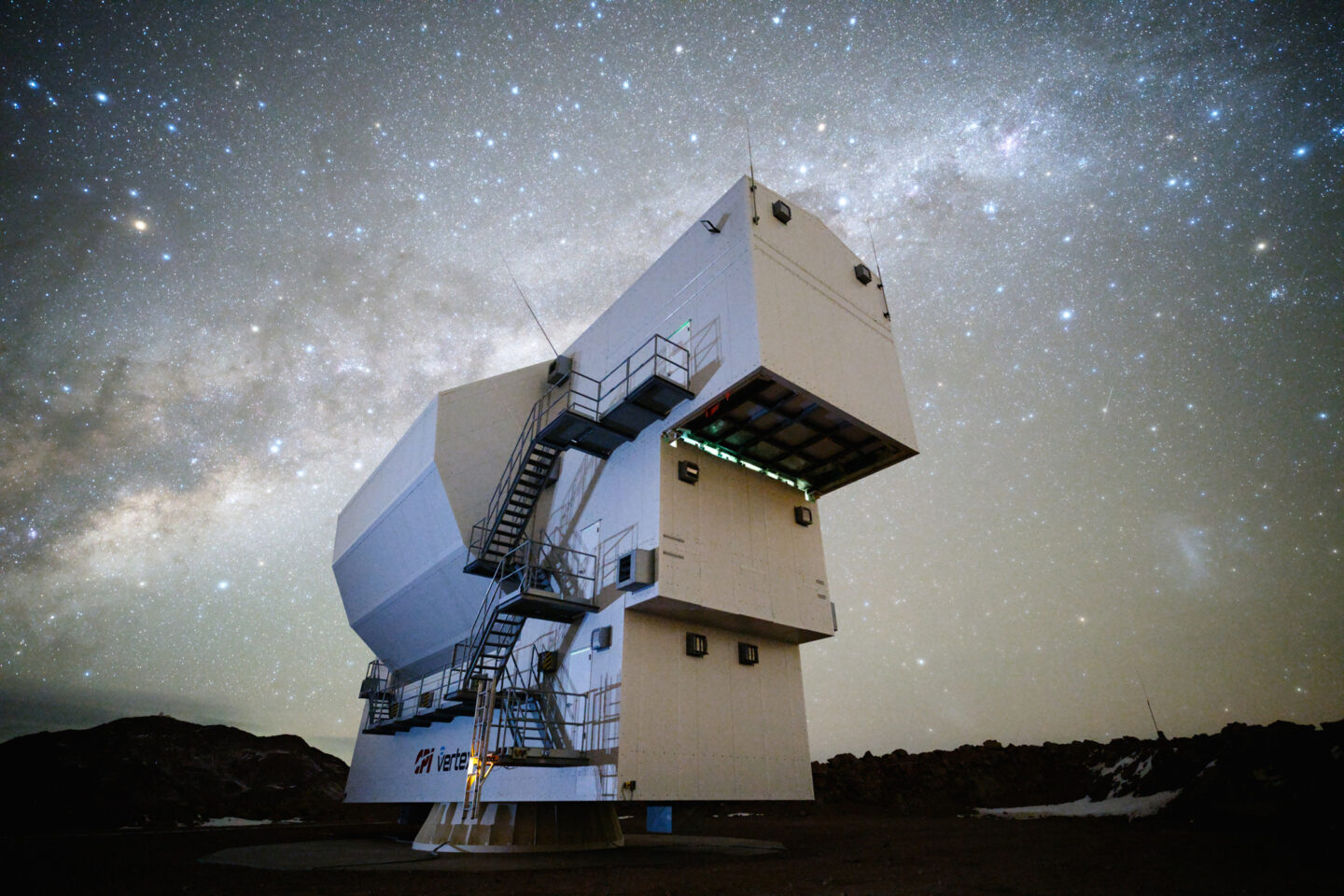 A large, rectangular radio telescope structure sits on a rocky landscape under a star-filled night sky.