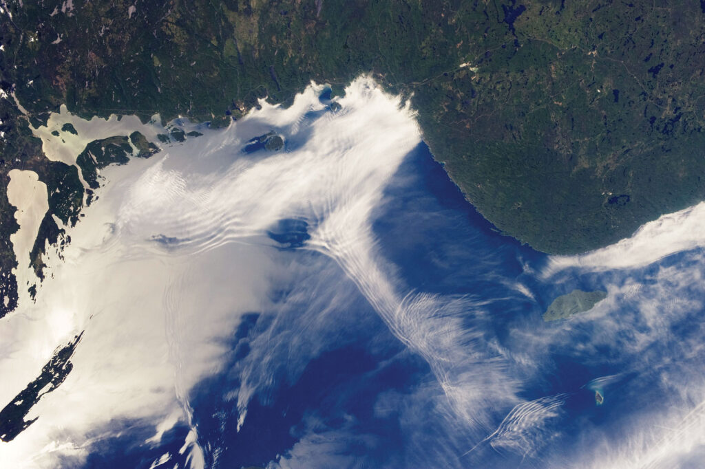 Satellite view of waves in the clouds off a forested coastline.