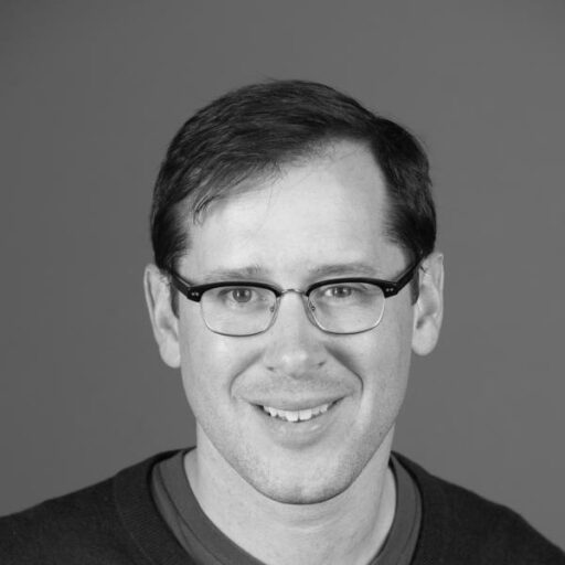 A headshot of a smiling man wearing glasses.