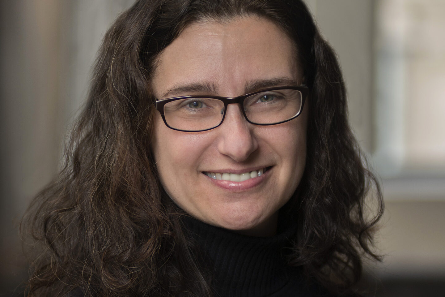 A woman with shoulder-length wavy hair and glasses smiling at the camera.