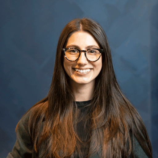 A woman with long dark hair and glasses smiling at the camera.