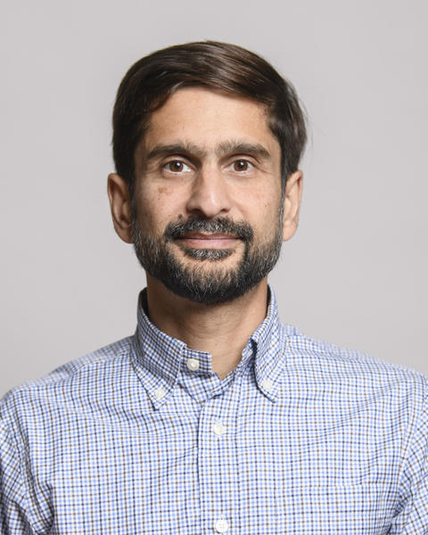 A man with a beard wearing a blue and white checkered button-down shirt.
