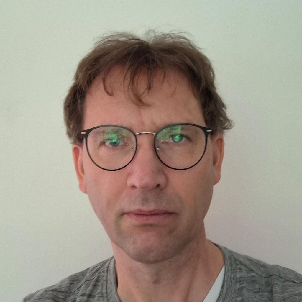 A middle-aged man with short brown hair and round glasses looking directly at the camera.