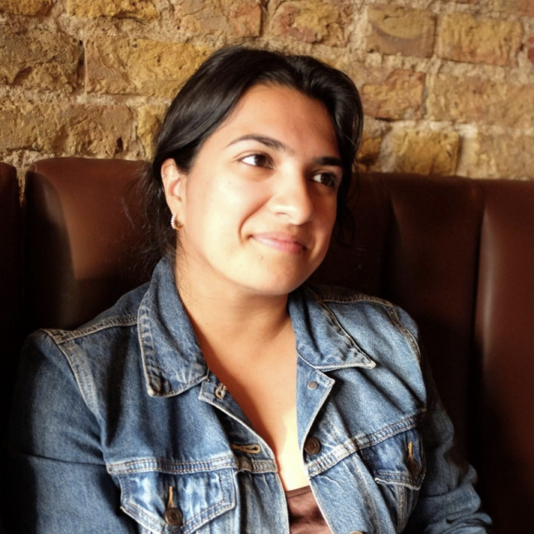 A woman wearing a denim jacket sits in a booth against a brick wall.