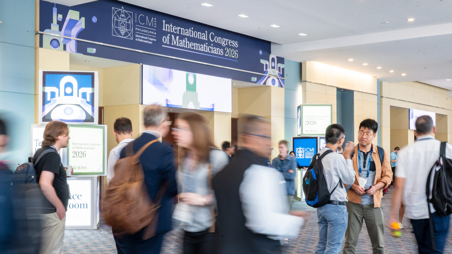 Attendees walk through a lobby area featuring signage for the International Congress of Mathematicians 2026.