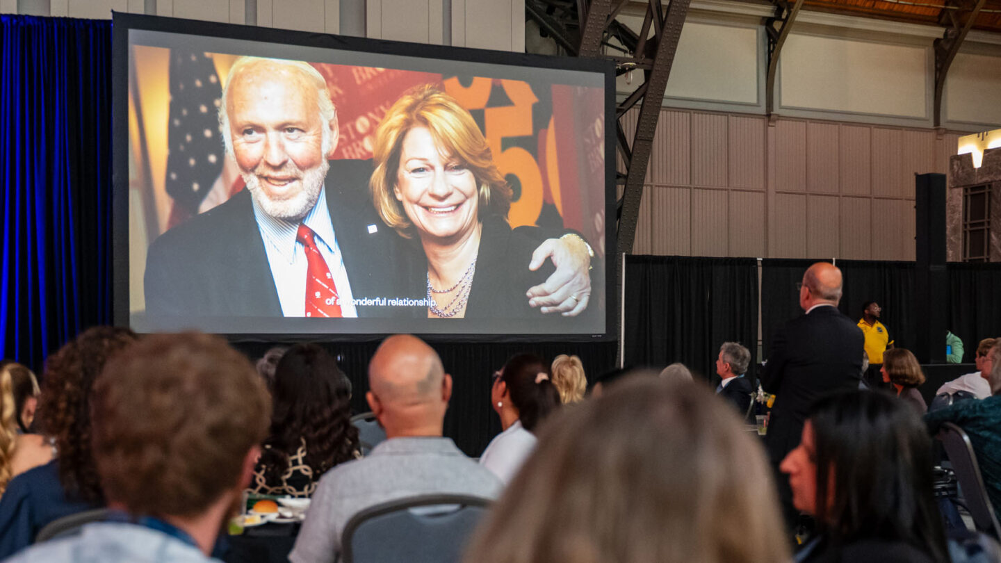 An audience views a large screen displaying a photo of a man and woman smiling together, with text at the bottom reading of a wonderful relationship.