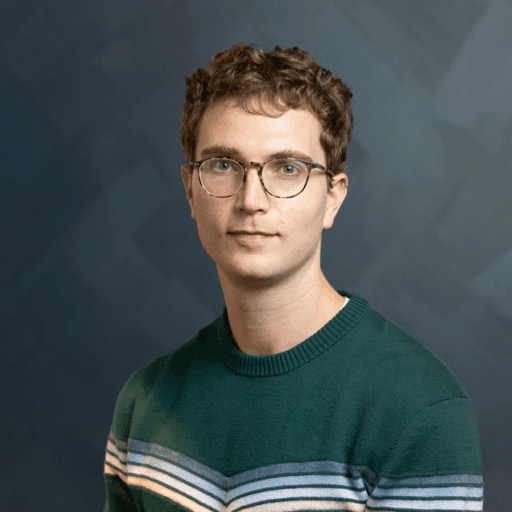 A person with short curly hair and glasses wearing a green striped sweater.