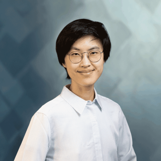 A person with short dark hair and round glasses wearing a light-colored button-down shirt.