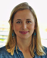 A woman with blonde hair wearing turquoise drop earrings and a denim shirt.
